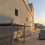 جدار خارجي جانبي لفيلا قيد التشطيب في الكويت نهاراً مع سقالة منخفضة وفتحات خارجية وعمال بخوذ أمان يظهرون من بعيد