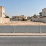 قسيمة سكنية مستوية بعد إزالة بيت قديم في الكويت مع حفارة متوقفة وسياج مؤقت وعمال بخوذ أمان من بعيد